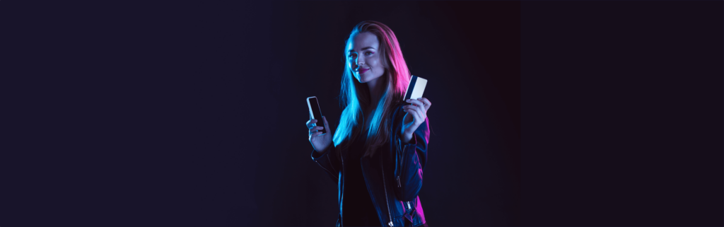 mulher sorrindo com cartão de crédito em uma mão e na outra um celular